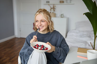 Portrait of smiling young woman eating food at home