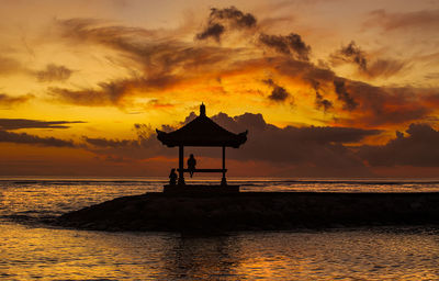 Silhouette people on gazebo at pier by sea against cloudy sky during sunset