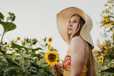 Portrait of beautiful young woman wearing hat standing against plants