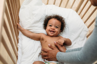 Cropped hand of mother touching smiling son in crib at home