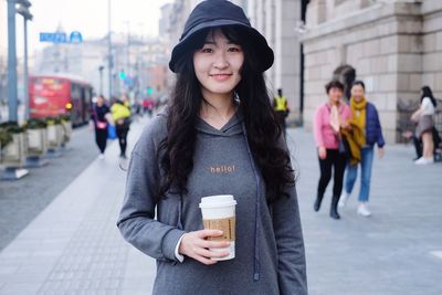 Portrait of beautiful woman holding coffee while standing on city street