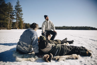 Father and son sitting on animal skin while ice fishing with friends enjoying sunny day in winter
