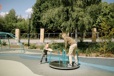 Boy with down syndrome spinning father on carousel at park during sunny day