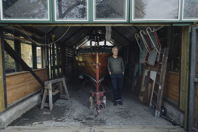 Senior man standing at wooden boat in a boathouse