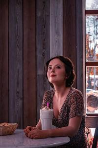 Smiling woman looking away while sitting by drink in glass on table