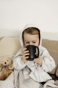 Sick little boy drinking hot tea on the bed at home. unwell, illness child wrapped in a blanket