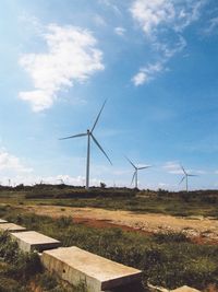 Wind turbines on field against cloudy sky