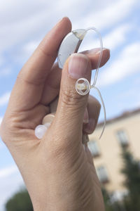Close-up of hand holding hearing aid outdoors against sky
