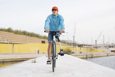 Young man with artificial limb and foot riding bicycle on footpath against clear sky