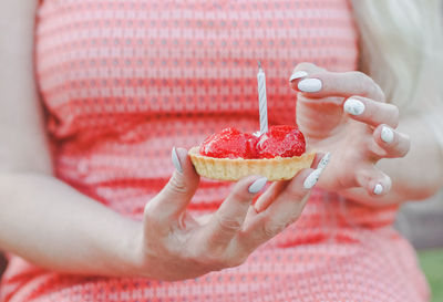 Portrait of a beautiful caucasian hand middle-aged woman holding a strawberry tartlet with a candle