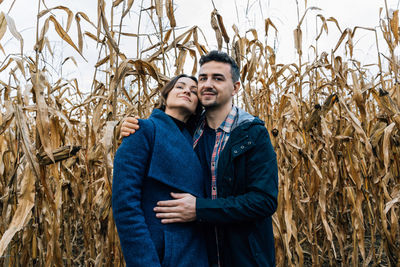 A young man hugs a woman standing against the backdrop of a cornfield in autumn