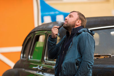 Man smoking pipe while leaning on car