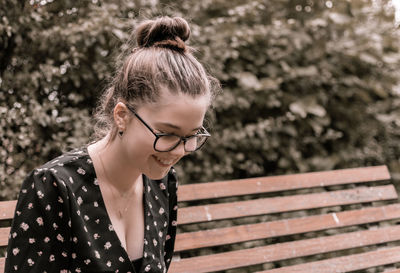 Close-up of young smiling woman sitting on bench outdoors