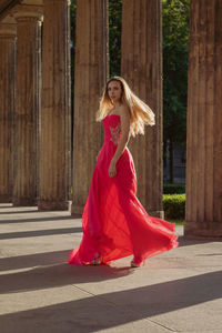 Full length side view of young woman in pink evening gown walking at colonnade