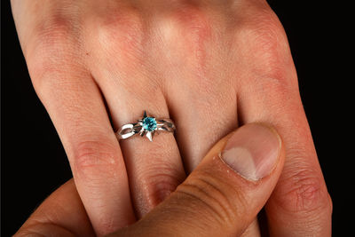 Cropped image of hand holding ring over black background