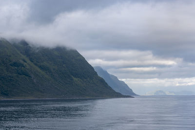 Scenic view of sea by mountain against sky