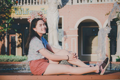 Full length portrait of woman sitting against building