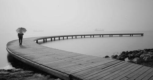 Rear view of woman standing on pier against sky