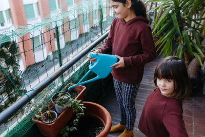 Two sisters with dark hair on apartment balcony watering the plants