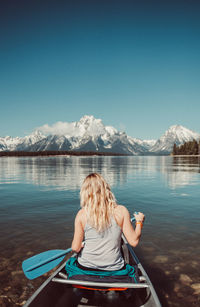 Rear view of woman sailing boat in lake against blue sky