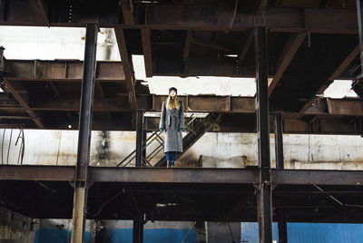 Young woman in warm clothes standing at abandoned building