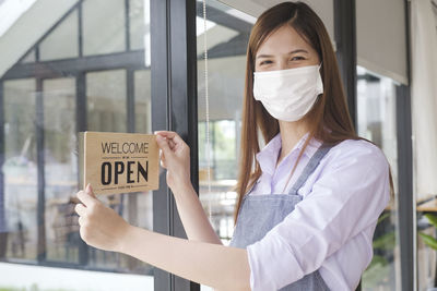 Portrait of woman holding open sign on glass window