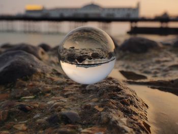 Close-up of glass ball on rock with brighton pier reflection