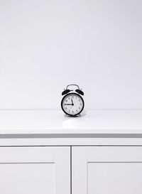 Alarm clock on cabinet against white wall