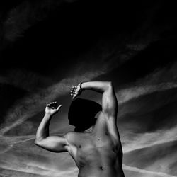 Rear view of shirtless man with arms raised against sky