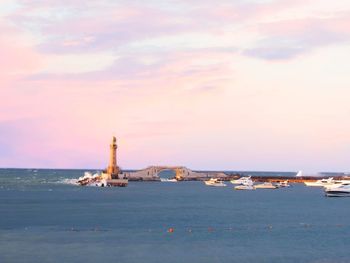 Lighthouse by sea against sky during sunset