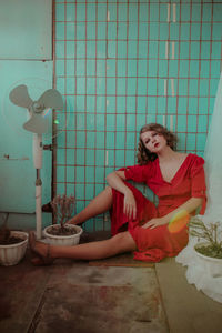 Young woman in red dress sitting against wall