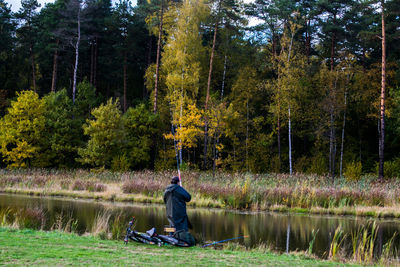 Full length of man sitting by lake in forest