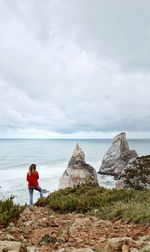 Woman standing on rock by sea against sky