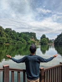 Rear view of man looking at lake against sky. 