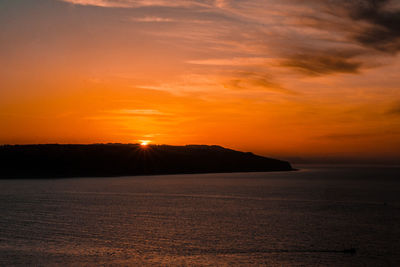 Scenic view of seascape by mountain during sunset