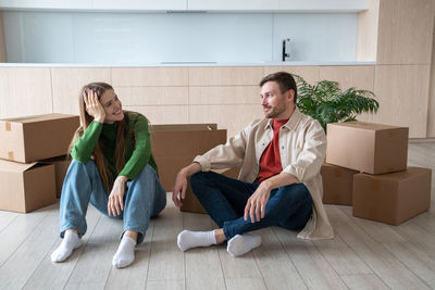 Couple man woman talking dreaming about living in new apartment sitting on floor between boxes.