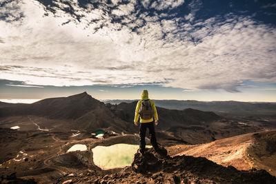 Rear view of man standing on rocky cliff against sky