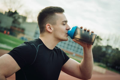 Young man drinking drink in glass bottle