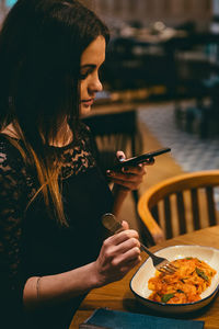 Woman using phone while eating food in restaurant