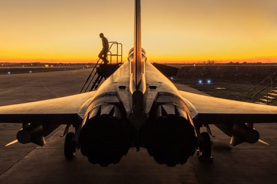 Airplane at runway against sky during sunset