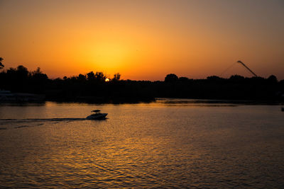 Silhouette person on river against sky during sunset