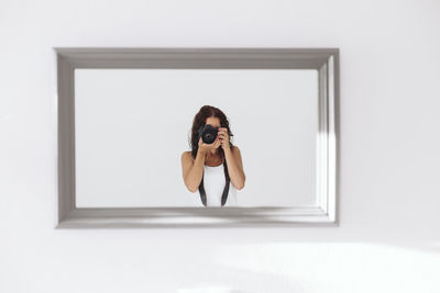 Portrait of woman photographing through window at home