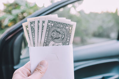 Cropped hand holding paper currency against car