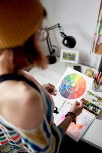 Side view of female artist standing at table with color wheel on paper while working on project in modern art studio