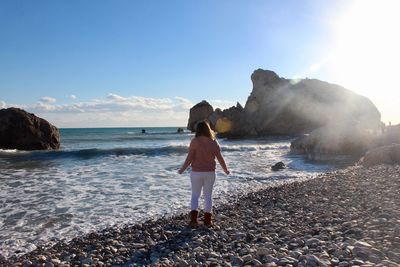 Rear view of woman standing on rock at beach against sky