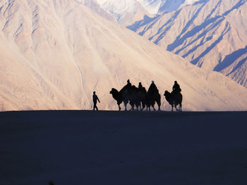 People riding camels on sand against mountains