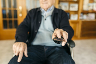 Hand of senior man sitting in wheelchair using remote control, close-up