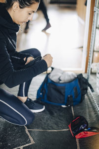 Side view of woman checking diabetes kit while kneeling on floor at home