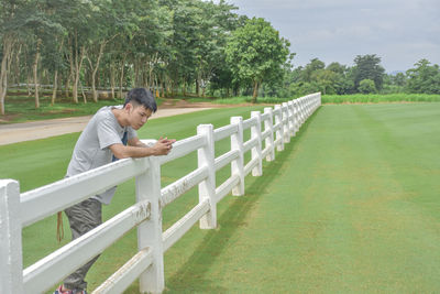 Young man leaning on fence outdoors