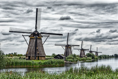 Traditional windmill by lake against sky